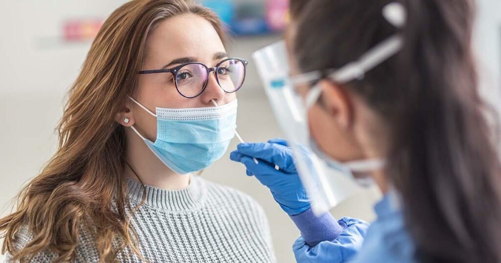 Female patient wearing mask over mouth is having sample taken from nose for a pcr test for Covid 19.