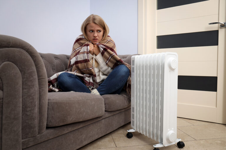 Heating season, woman sitting on sofa and warm up with heater